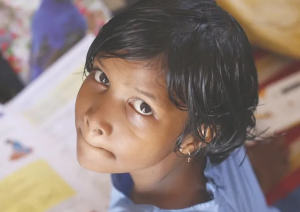 Portrait d’une enfant qui lève les yeux au-dessus de cahiers illustrés.