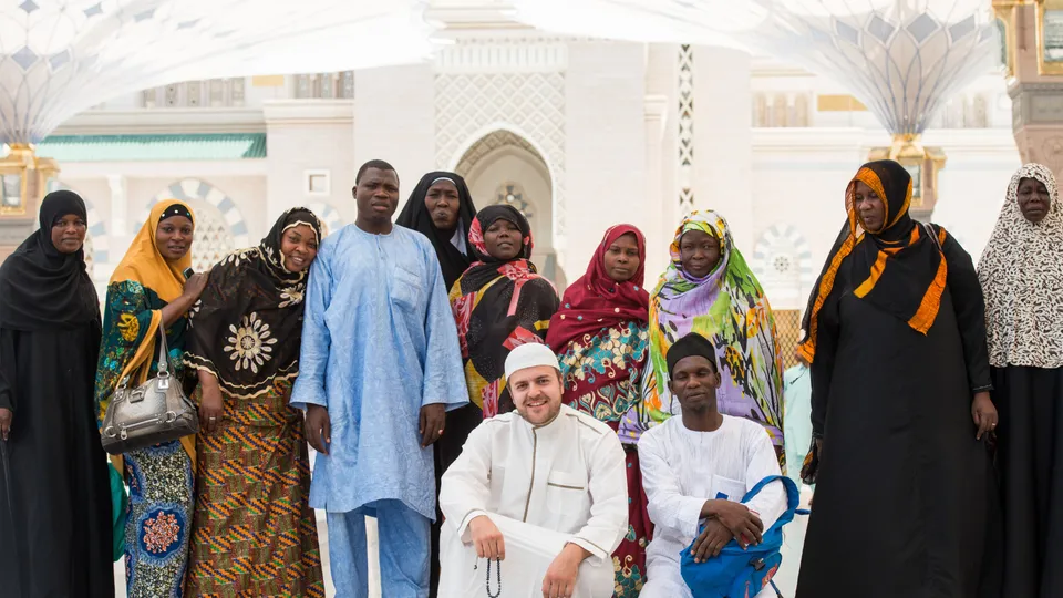 Photographie de groupe d'une quinzaine d'adultes, femmes et hommes en tenues colorées, posant devant un bâtiment blanc.