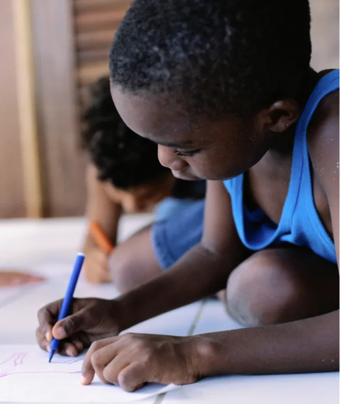 Deux enfants allongés sur le sol dessinent au crayon de couleur sur de grandes feuilles blanches.